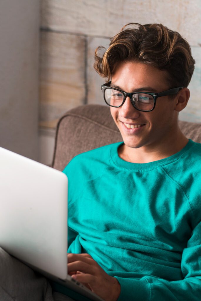 Young caucasian student study at home with internet and laptop computer sitting on the couch - home school concept - video conference and communicating people - happy boy